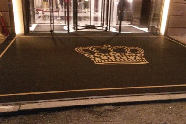 Custom gold crown logo mat at a luxury hotel entrance at night