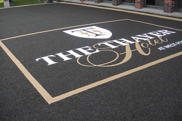A large exterior hotel mat sits outside the The Thayer with its logo prominently featured.